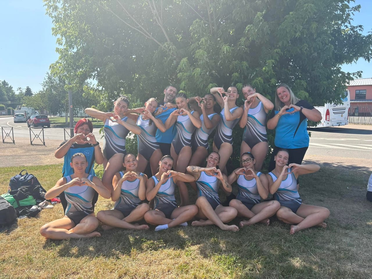 Les gymnastes et les entraîneurs de L’Envol de Feurs réunis en extérieur, formant un cœur avec les mains après une compétition.